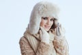 smiling woman in winter coat and fur hat touching face on white Royalty Free Stock Photo