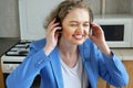 Smiling woman in wireless headset sit at desk in kitchen online on laptop, happy young female in headphones watch webinar or