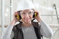 Smiling woman worker portrait wearing helmet, safety glasses and hearing protection headphones, scaffolding interior construction