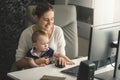 Smiling woman working at computer with her little baby son Royalty Free Stock Photo