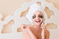 Smiling woman wrapped in towel after bath and with black eye patches is relaxing on the bed and talking on the phone. Beauty Royalty Free Stock Photo