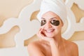 Smiling woman wrapped in towel after bath and with black patches under eyes is posing on the bed. Beauty treatment concept Royalty Free Stock Photo