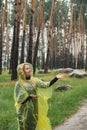 Smiling woman in yellow raincoat walking in autumn forest enjoying rainy weather outdoors. Female tourist discover park Royalty Free Stock Photo