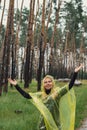 Smiling woman in yellow raincoat walking in autumn forest enjoying rainy weather outdoors. Female tourist discover park Royalty Free Stock Photo