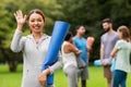 Smiling woman with yoga mat waving hand at park Royalty Free Stock Photo