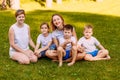 Smiling women and children sit on the green grass. Big happy family, two mothers and three children in white t-shirts. Summer Royalty Free Stock Photo