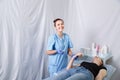 Smiling woman doctor beautician stands next to a massage table and holds a hand to a young woman, General plan,