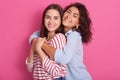 Smiling women embracing and looking directly at camera. Lesbian couple or women friendship concept. Isolated front view over pink