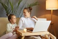 Smiling woman with her little kid posing at home mother with daughter watching movie together on laptop while sitting on sofa Royalty Free Stock Photo