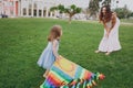 Smiling woman in light dress and little cute child baby girl play with colorful kite on grass in green park. Mother Royalty Free Stock Photo