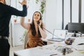 Cheerful businesswoman high-diving colleague while on phone in modern office with laptop and charts.