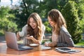 Smiling women sitting outdoors in park drinking coffee using laptop Royalty Free Stock Photo