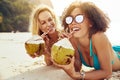 Smiling women suntanning on a beach and drinking from coconuts