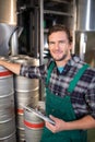Smiling worker holding clipboard while standing by kegs at warehouse Royalty Free Stock Photo