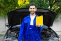 Smiling worker holding yellow container of motor oil near modern car Royalty Free Stock Photo