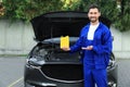 Smiling worker showing yellow container of motor oil near car outdoors Royalty Free Stock Photo