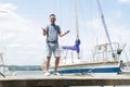 A Smiling Yachtsman portrait on pier with both thumbs up. river and yachts on background. Young successful man sailor on pier