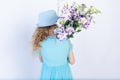 A smiling 5-6-year-old girl in a blue dress and hat on a white isolated background holds a bouquet of flowers, space for text Royalty Free Stock Photo