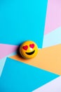 Smiling yellow emoticon with heart eyes, on multicolored geometric texture