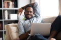 Smiling young adult african guy using laptop relaxing on sofa Royalty Free Stock Photo