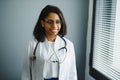 Smiling young adult indian female doctor wear white coat in medical clinic office. Happy beautiful health care india Royalty Free Stock Photo