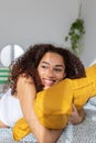 Smiling young adult woman hugging yellow pillow relaxing on bed at home Royalty Free Stock Photo
