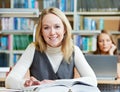 Smiling young adult woman reading book in library