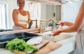 Smiling young adult woman washing fish under the kitchen sink water tap. Healthy seafood preparation and house work concept image Royalty Free Stock Photo