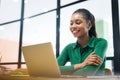 Smiling young african-american business woman wearing casual shirt using laptop for office work, female employee checks Royalty Free Stock Photo
