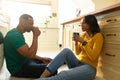 Smiling young african american couple drinking coffee while sitting on kitchen floor at home Royalty Free Stock Photo