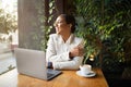 Smiling young african american female in suit with smart watch works with laptop, enjoy cup of coffee