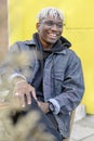 Smiling young African American man with dreadlocks sits on the street and have fun. Happy melinial generation Royalty Free Stock Photo