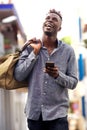 Smiling young african american man with handbag walking outside with mobile phone Royalty Free Stock Photo