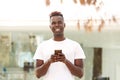 Smiling young african american man with mobile phone standing outside in city Royalty Free Stock Photo