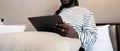 Smiling young African American man using digital tablet remote job sitting on the bed at home. concept online technology Royalty Free Stock Photo