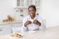 Smiling young african american woman with cup of coffee in hands drinks favorite drink with cookies Royalty Free Stock Photo