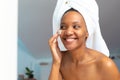 Smiling young african american woman with head wrapped in towel applying face cream, copy space