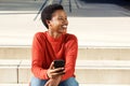 Smiling young african american woman sitting outside with mobile phone Royalty Free Stock Photo