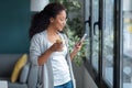 Smiling young african american woman using her mobile phone while sitting on sofa at home Royalty Free Stock Photo