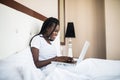 Smiling young african american woman using laptop on bed at home Royalty Free Stock Photo