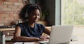 Young African American woman in earphones confer online using laptop