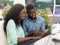 Smiling young african couple having fun looking at smartphone in cafe terrace Royalty Free Stock Photo