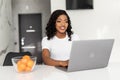 Smiling young African entrepreneur working online with a laptop while sitting at her kitchen table at home Royalty Free Stock Photo