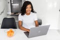 Smiling young African entrepreneur working online with a laptop while sitting at her kitchen table at home Royalty Free Stock Photo