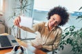 Smiling young African female entrepreneur sitting at a desk in her home office make selfie Royalty Free Stock Photo