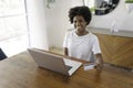 Smiling young African female entrepreneur working online with a laptop while sitting at her kitchen table at home Royalty Free Stock Photo