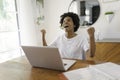 Smiling young African female entrepreneur working online with a laptop while sitting at her kitchen table at home Royalty Free Stock Photo