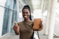 Smiling young african girl hold passport boarding pass tickets showing thumb up in airport terminal Royalty Free Stock Photo