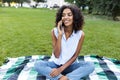 Smiling young african girl sitting on grass outdoors in park talking by phone. Royalty Free Stock Photo