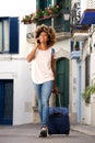 Smiling young african woman traveling with bag and mobile phone on street Royalty Free Stock Photo